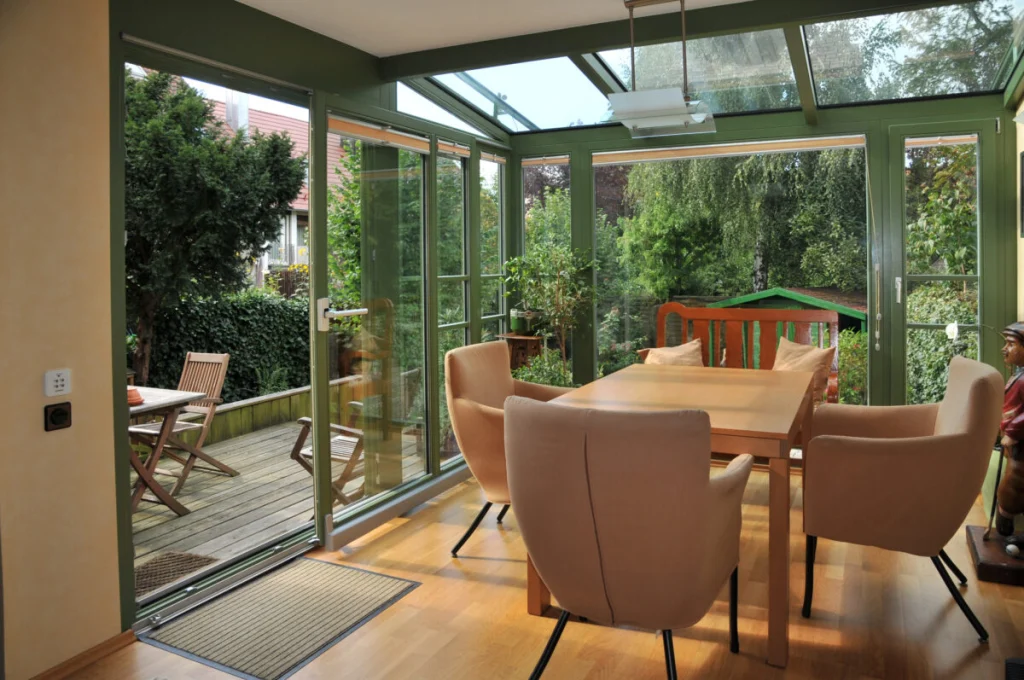 Esszimmer im Wintergarten in Schoppershof mit grünen Rahmen, Glasdach und offener Schiebetür zur Holzterrasse