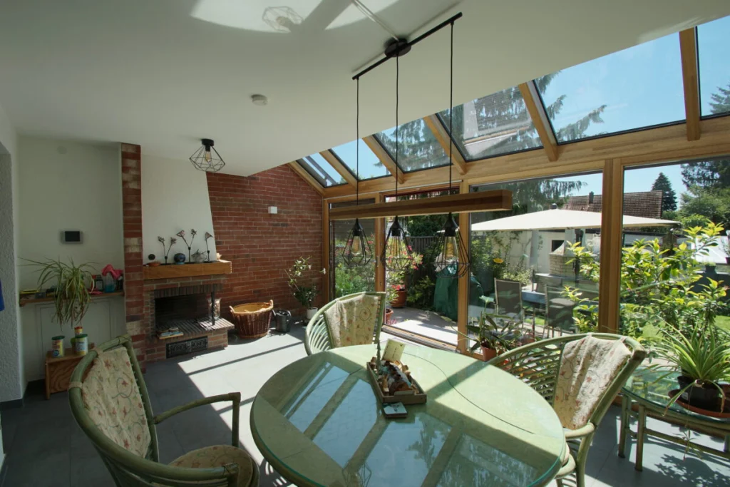 Wintergarten in Ahorntal, Holzkonstruktion mit Glasdach, Klinkerkamin, Rattanmöbel und Blick auf Terrasse und Garten