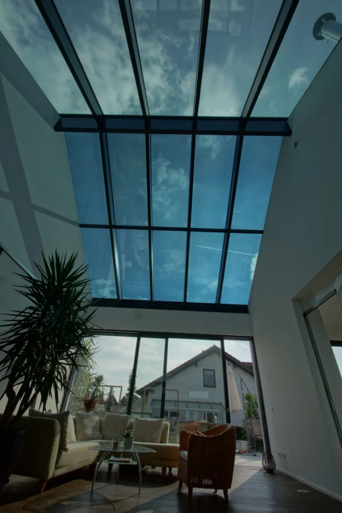 Glasdach in Buckenreuth von innen, beide Dachhälften verglast, dunkle Sparren, Sofa und Schiebetür mit Blick auf Nachbarhaus