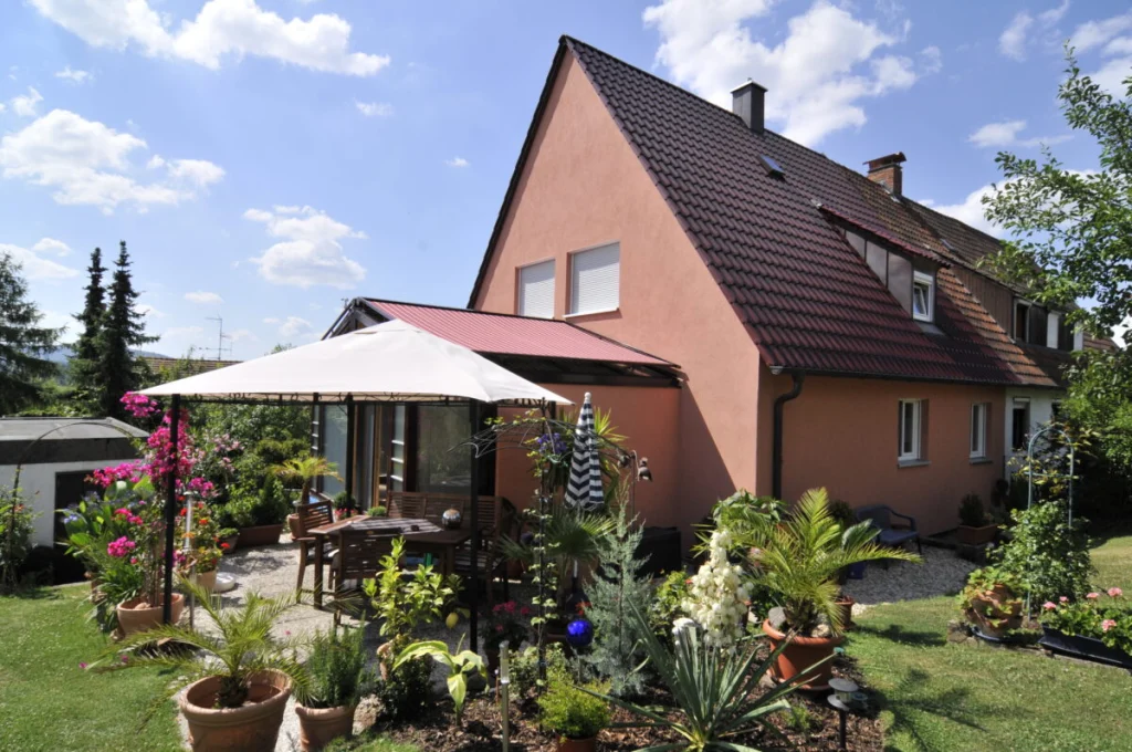 Wohnhaus in Burk mit Wintergarten, roter Dachmarkise und Pavillon auf der Terrasse im Sommer