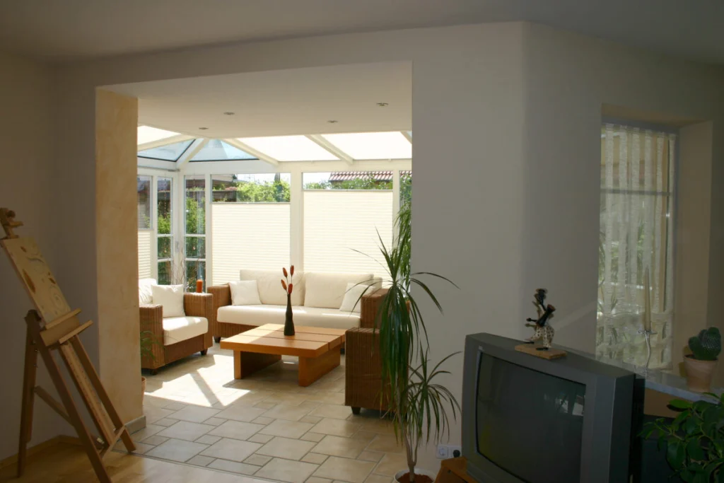 Blick aus dem Wohnzimmer in den Wintergarten in Hausen, offener Wanddurchbruch, Plissees an den Scheiben