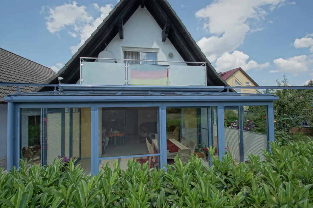 Wintergarten in Herpersdorf von außen, Pultdach-Anbau mit blaugrauen Profilen unter dem Balkon eines Hauses mit Satteldach