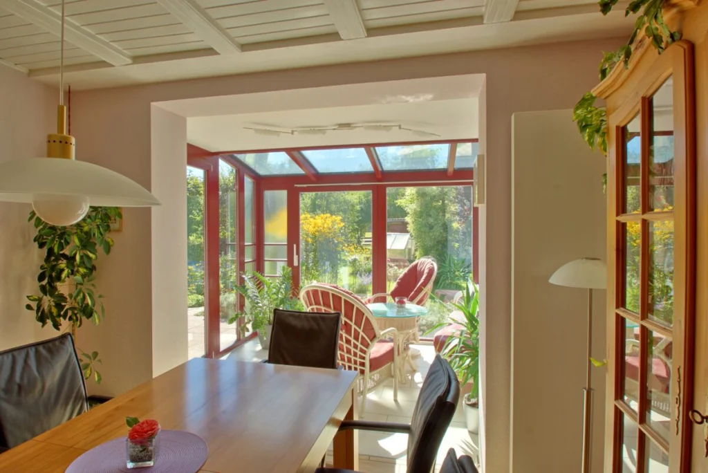 Blick vom Esszimmer in den Wintergarten in Hormersdorf, Holztisch mit schwarzen Stühlen, Korbmöbel und Glasdach dahinter