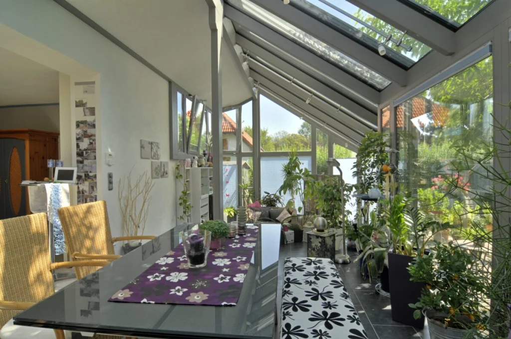 Wintergarten in Kleinsendelbach von innen, geschlossener Dachteil am Haus geht in Glasdach über, Glastisch und Pflanzen