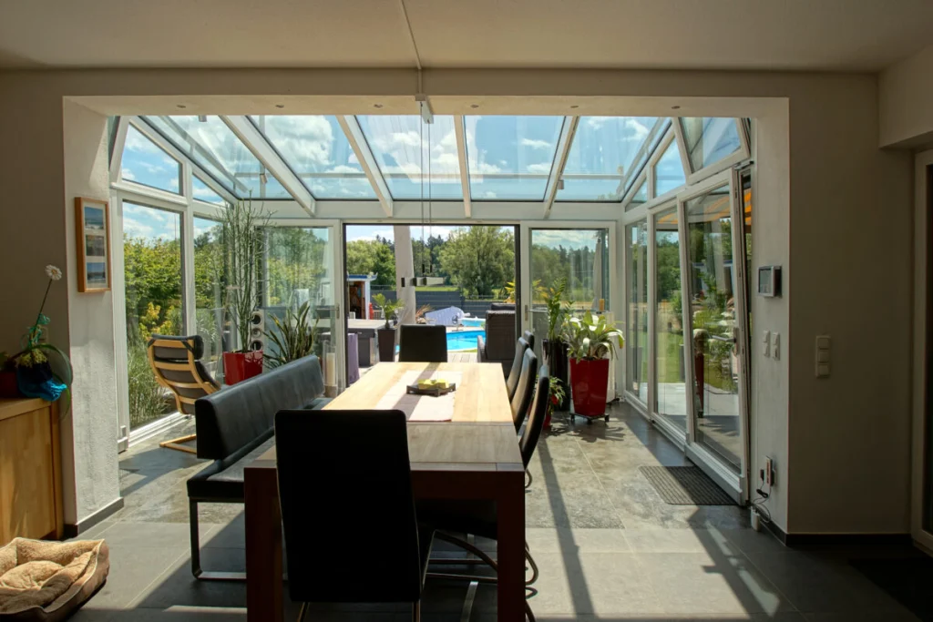 Wintergarten in Königsfeld vom Wohnraum aus, Glasdach mit weißen Profilen, Esstisch und Blick auf den Pool
