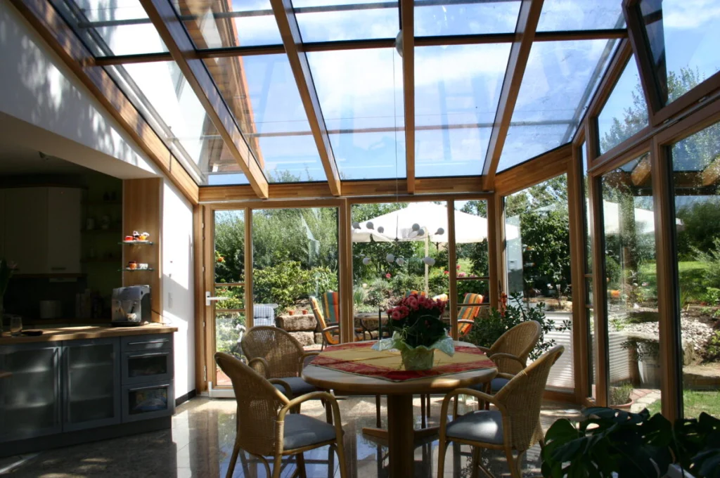 Wintergarten in Kunreuth von innen, Glasdach mit Holzsparren, runder Esstisch, offene Küche und Blick in den Garten