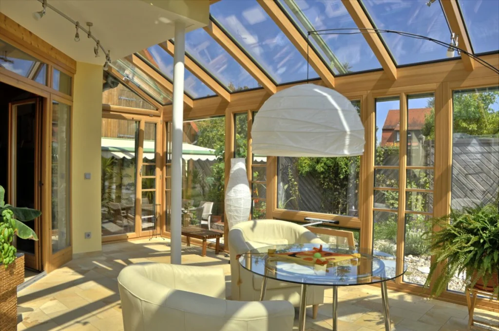 Wintergarten in Lauf von innen, Holzsparren mit Glasdach, weiße Ledersessel, Glastisch und Tür zur Terrasse