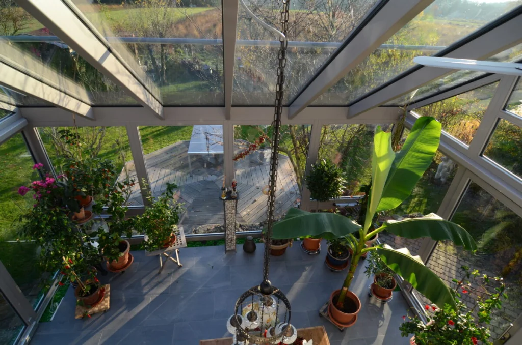 Blick von der Galerie in den Wintergarten in Möhrendorf, Glasdach, Kübelpflanzen, Mosaikleuchte und Holzdeck im Garten
