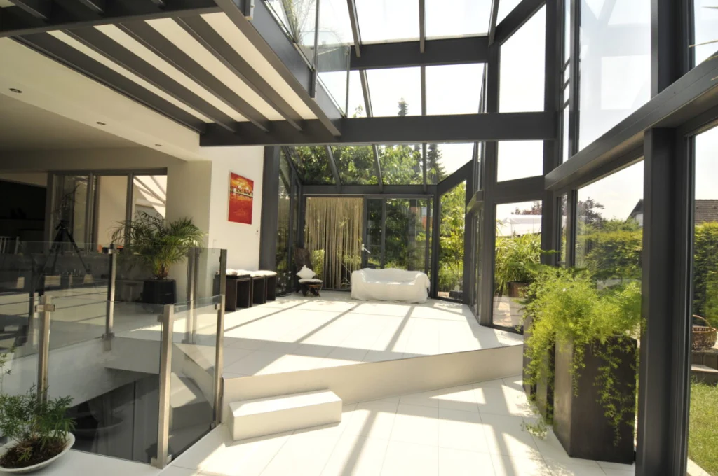 Wintergarten in Baiersdorf als Wohnraum mit weißem Sofa, weißen Fliesen und Blick durch die Glasfassade in den Garten