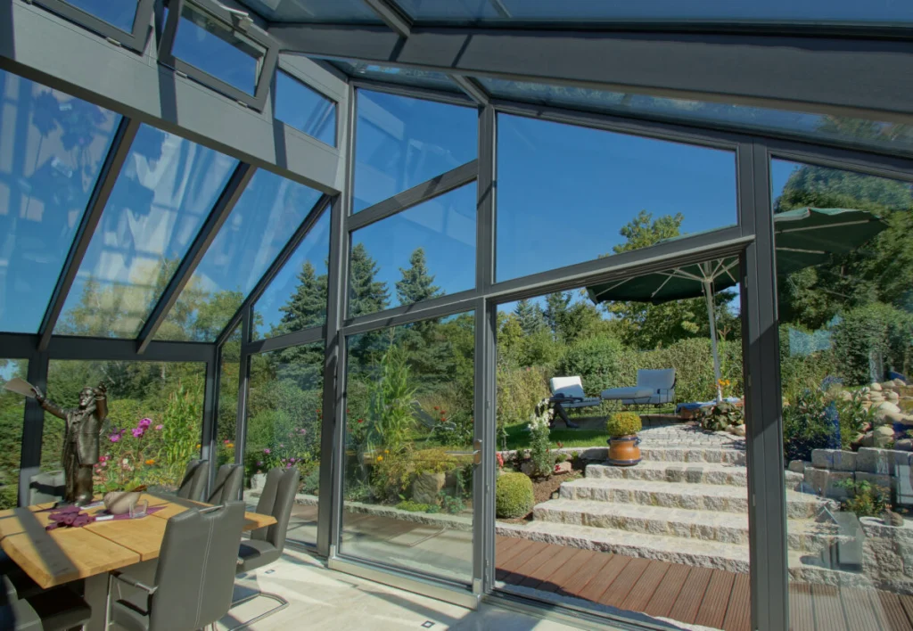Wintergarten in Bayreuth, offene Schiebetür zur Holzterrasse mit Natursteintreppe, Sonnenschirm und Liegen im Garten