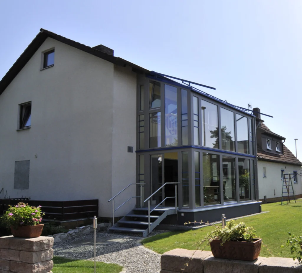 Wintergarten in Hannberg von außen, zweigeschossiger Glasanbau mit grauen Profilen an der Giebelseite eines Wohnhauses