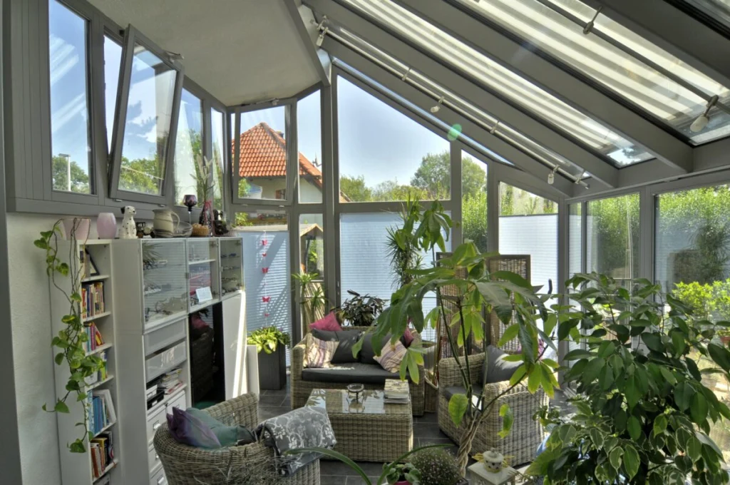 Wintergarten in Kleinsendelbach von innen mit gekippten Fenstern, Glasdach, Rattanmöbeln, Regal und Pflanzen