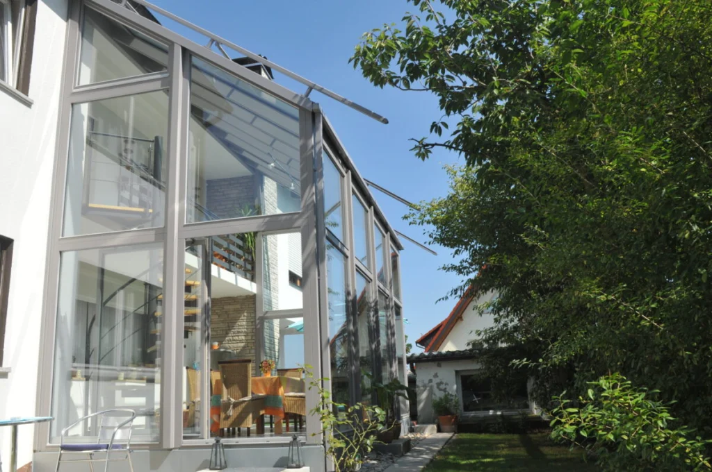 Wintergarten in Leutenbach über zwei Geschosse mit grauen Profilen und Pultdach an weißem Haus, Blick vom Garten