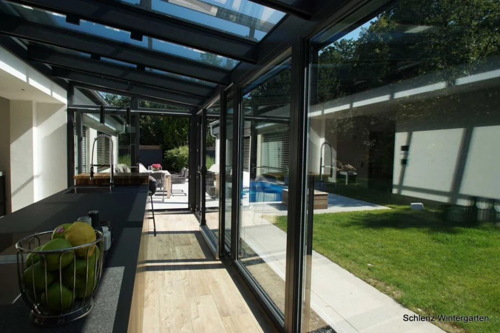 Wintergarten in Rathsberg innen, Blick entlang der Küchenzeile durch offene Glastüren zur Terrasse mit Pool