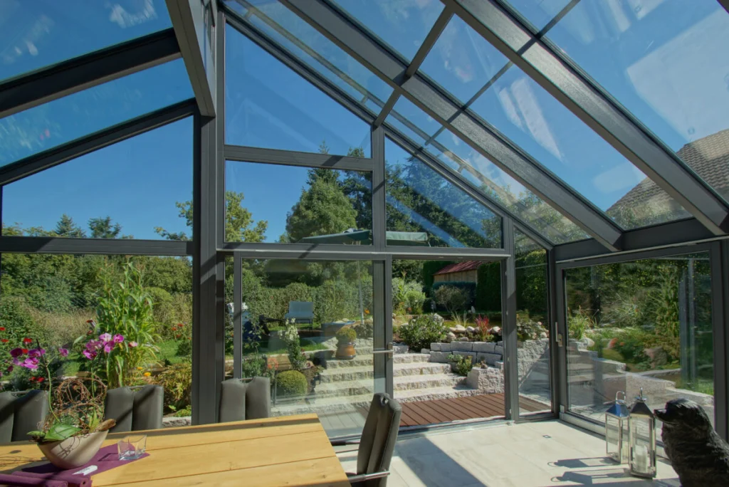 Wintergarten in Bayreuth, Satteldach aus Glas von innen mit grauen Sparren und Blick auf Terrasse und Hanggarten