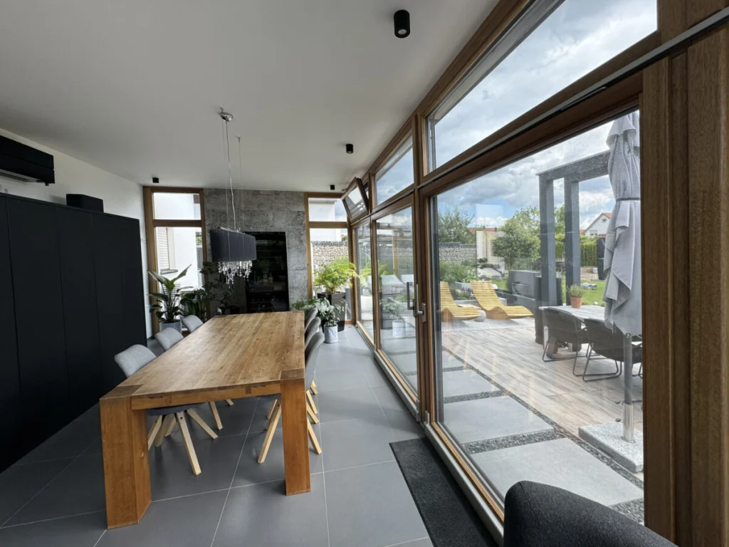 Anbau in Benzendorf von innen mit Eichentisch und Blick durch die Glasfront auf Holzterrasse und Pergola