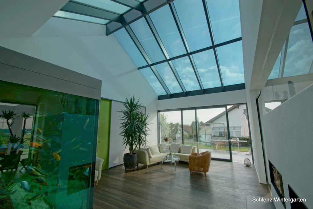 Wohnraum in Buckenreuth mit Glassatteldach, Aquarium, Palme, Sofa und Schiebetür zur Terrasse