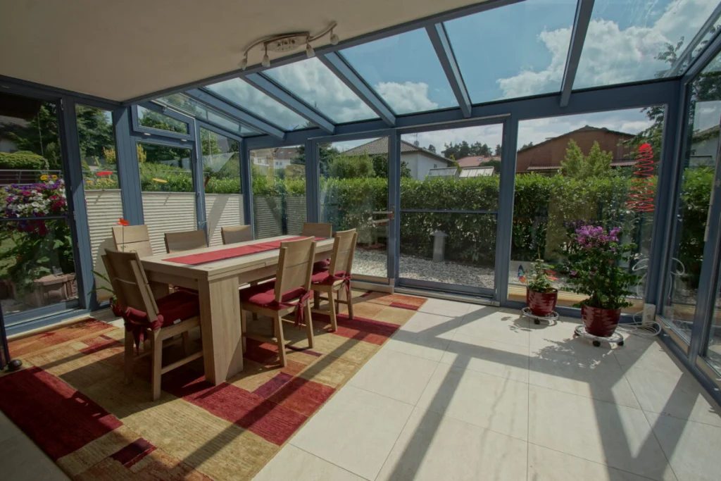 Wintergarten in Herpersdorf als Esszimmer mit Glasdach und blaugrauen Profilen, Blick in den Garten mit Hecke