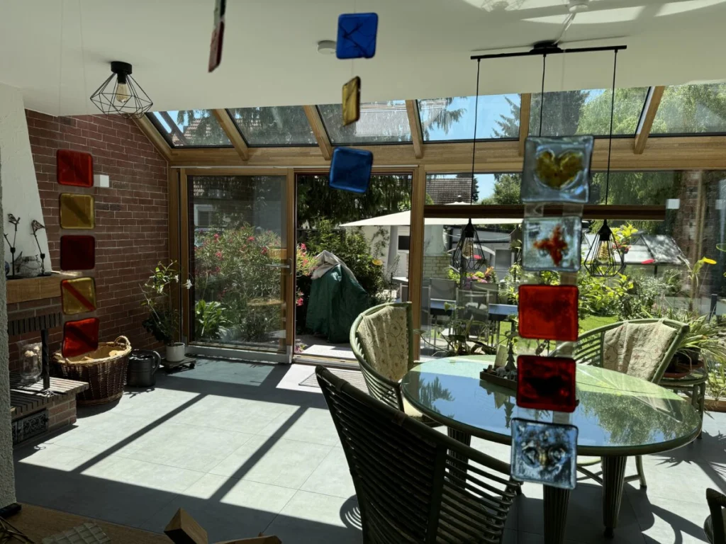 Wintergarten in Ahorntal innen mit Glasmobile, Klinkerkamin, Holzkonstruktion und offener Terrassentür