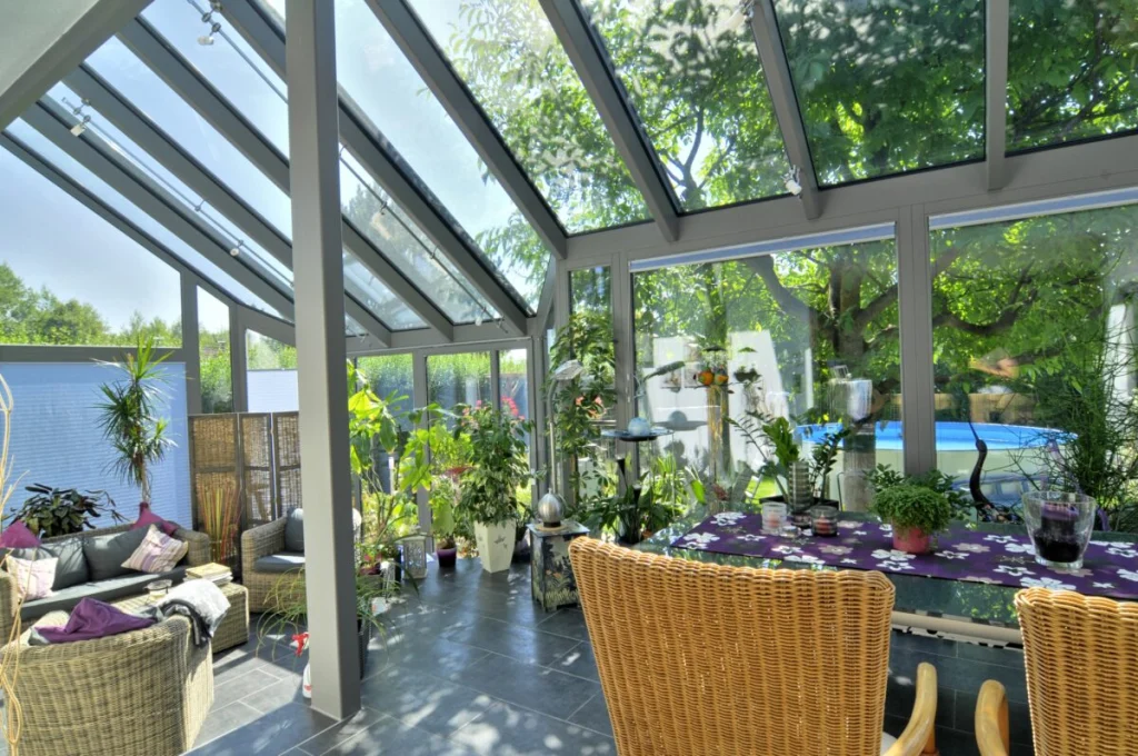 Wintergarten in Kleinsendelbach von innen, graues Glasdach mit Beschattung, Rattanmöbel, Pflanzen und Blick zum Pool