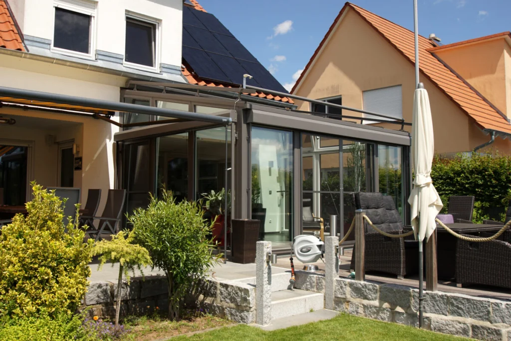 Wintergarten in Königsfeld, Außenansicht von der Seite mit Pultdach, Markise und Holzterrasse