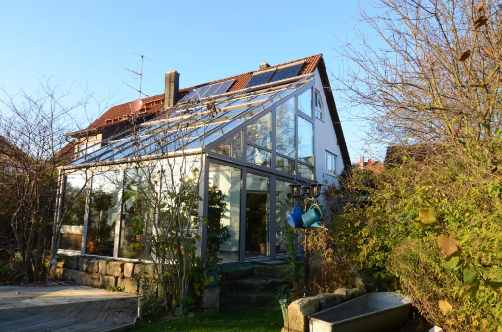 Zweigeschossiger Wintergarten in Möhrendorf mit Pultdach am Haus mit Solaranlage, Garten mit Holzdeck im Herbst