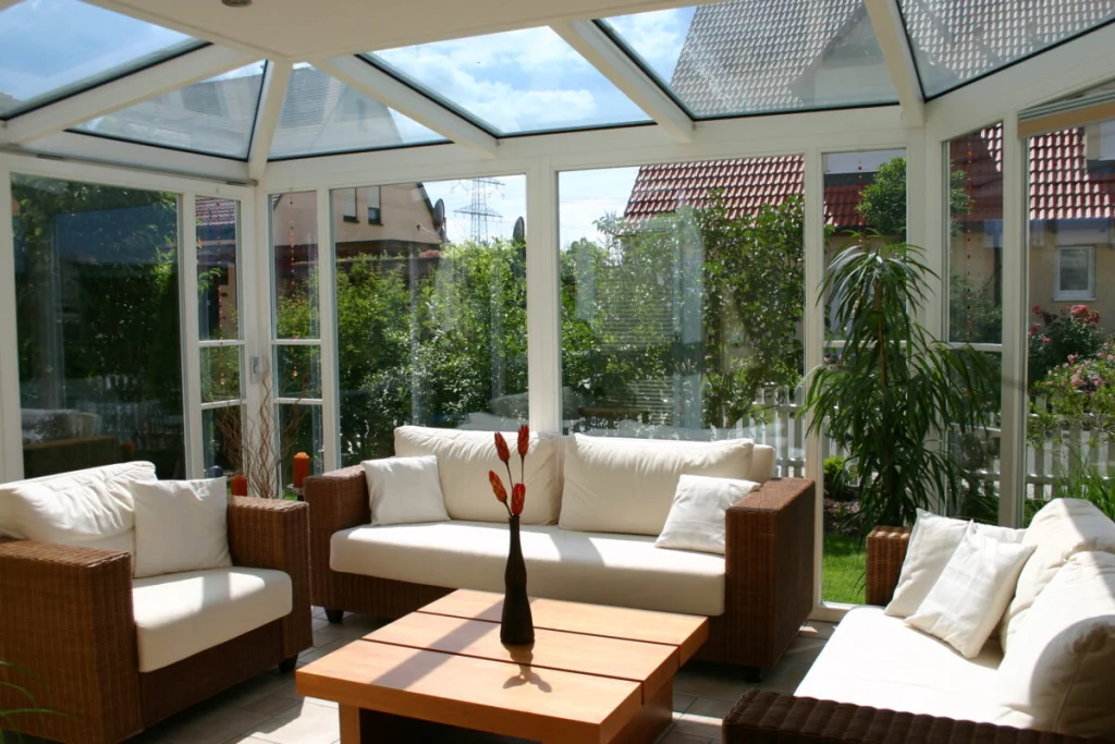 Wintergarten in Hausen von innen, weißes Glasdach mit Walm, Rattansofas und Blick auf Garten und Nachbarhäuser