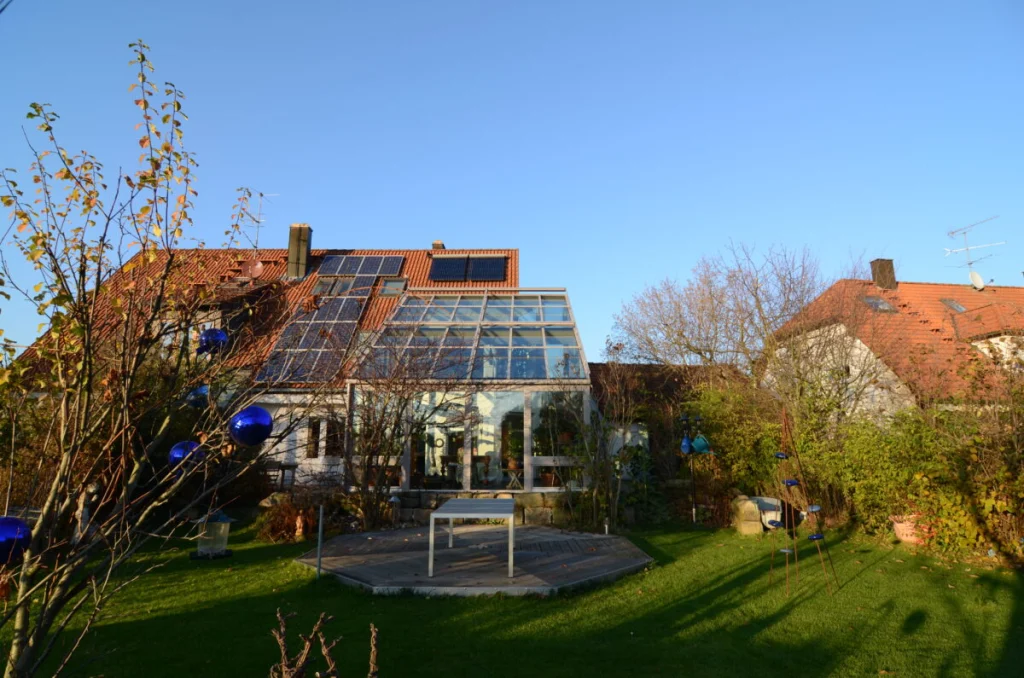 Zweigeschossiger Wintergarten in Möhrendorf mit Pultdach über der Trauflinie, Garten im Herbst mit Holzdeck