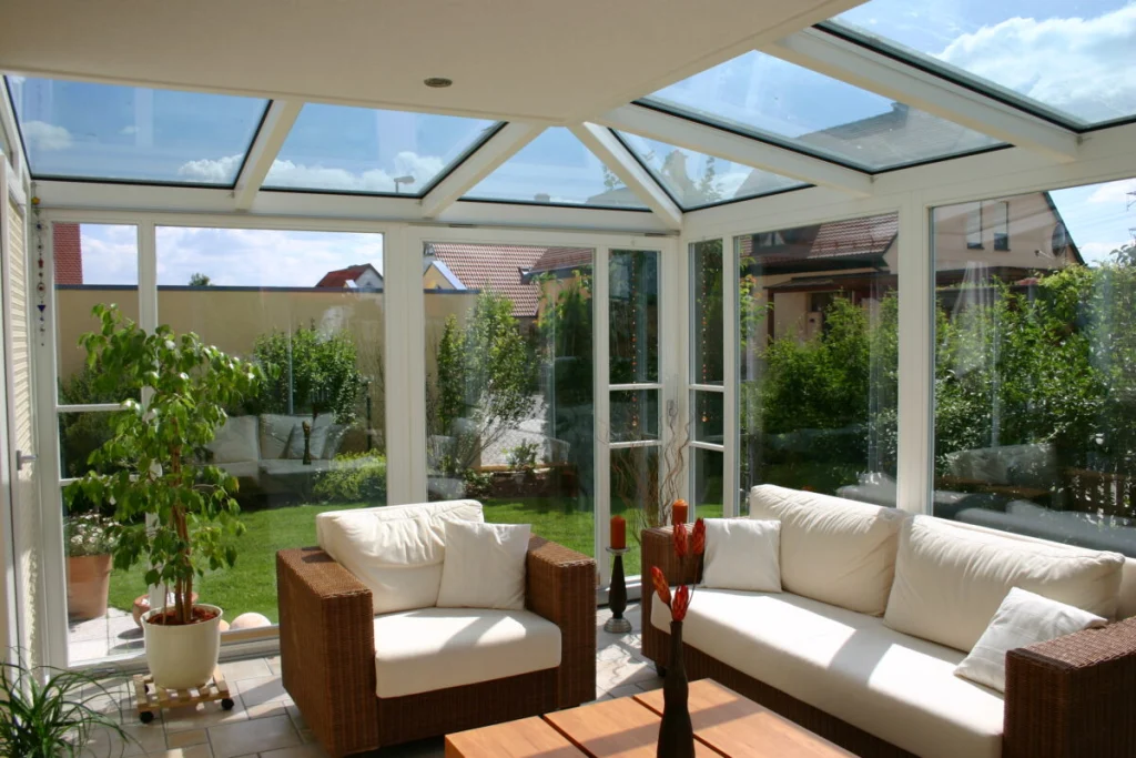 Wintergarten in Hausen von innen mit Glasdach, Fenstertür, Rattansofa und Blick auf den Rasen