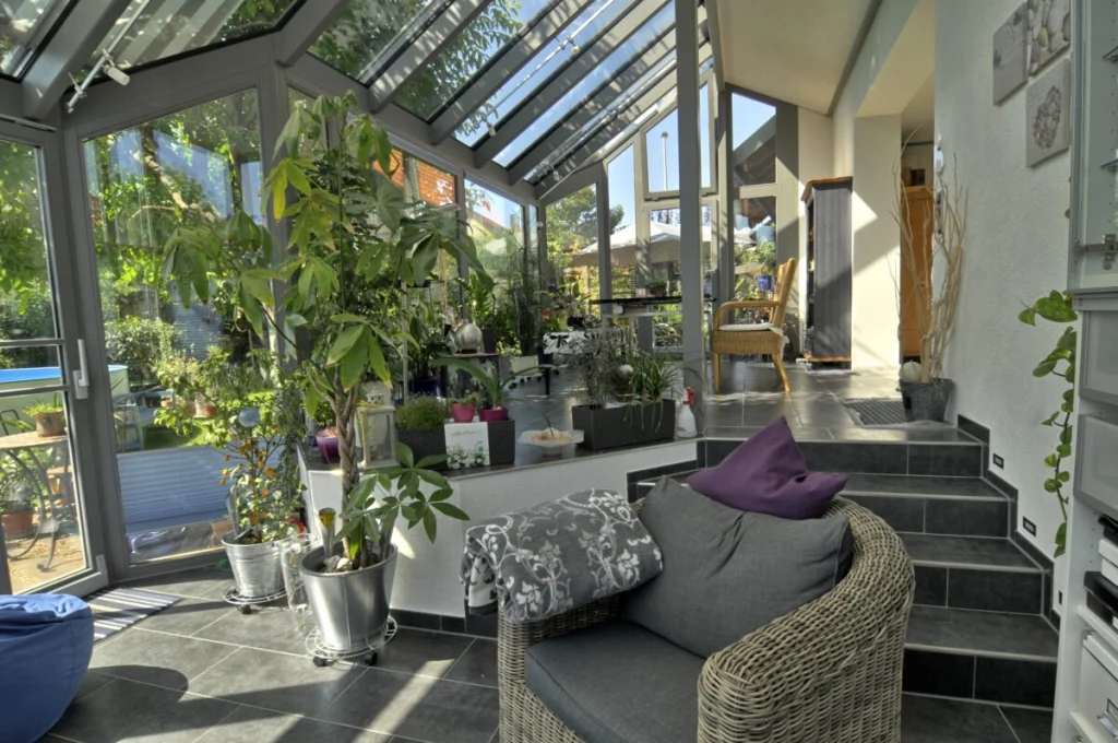 Wintergarten in Kleinsendelbach von innen mit Sitzecke, Rattansessel, Pflanzen, Treppe zum Haus und Glasdach