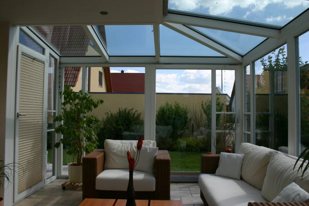 Wintergarten in Hausen von innen, Glasdach und Fenstertür, Rattansofas, Blick auf Nachbarhäuser
